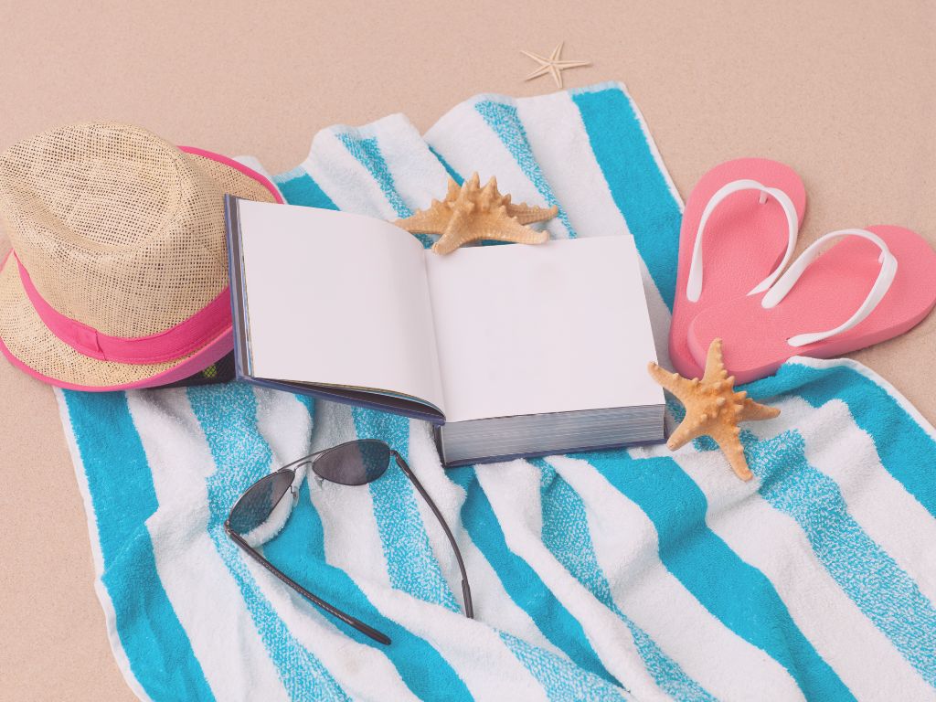 Carnet ouvert posé sur une serviette à la plage, avec un stylo et un coquillage