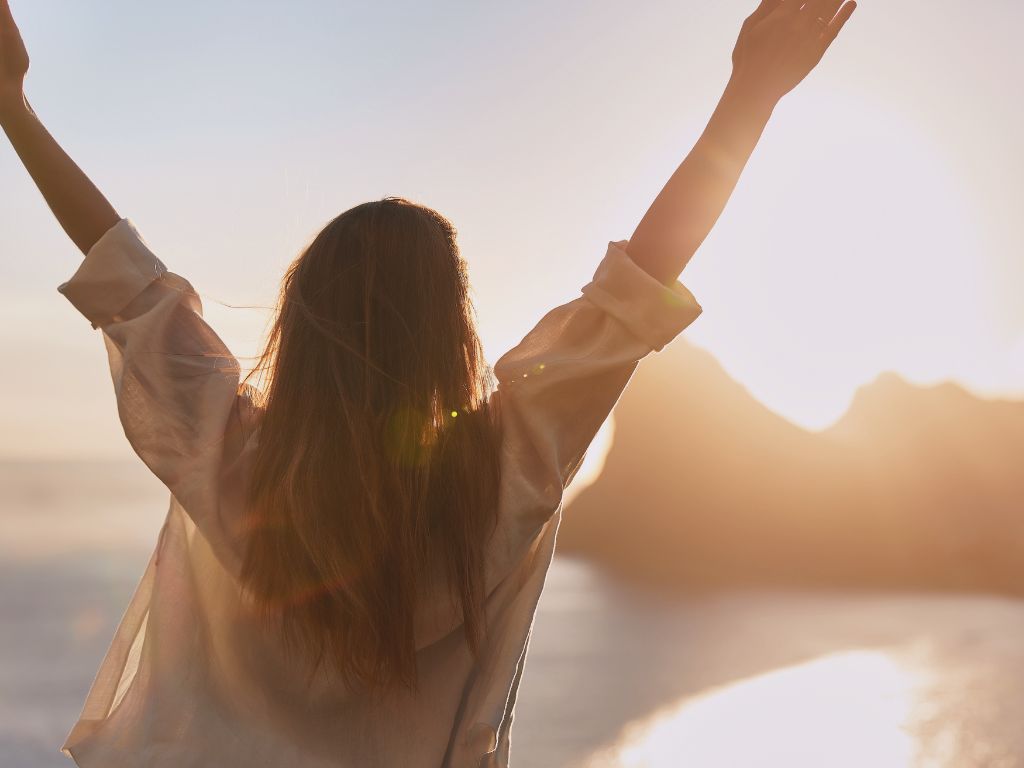 Femme debout face à la mer, bras ouverts au crépuscule