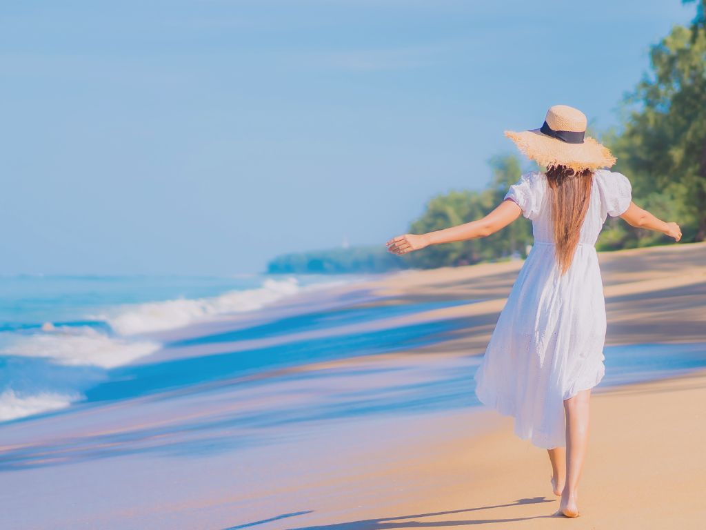 Femme en robe fluide marchant seule sur une plage déserte, dans une lumière douce du matin