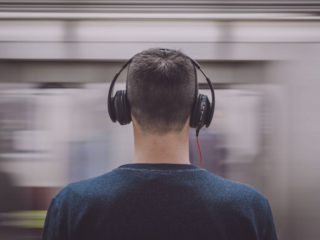 Personne debout, casque audio sur les oreilles, devant un tram flou lumineux