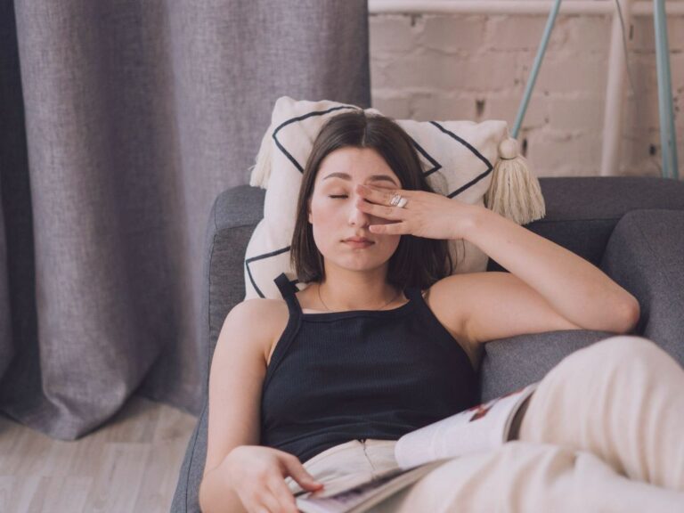 Femme allongée sur un canapé, main sur le front, air épuisé, préserver son énergie septembre