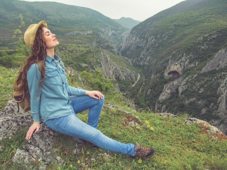 Femme assise sur un pente de montagne, yeux fermés, inspirant profondément, symbole de se choisir avec douceur