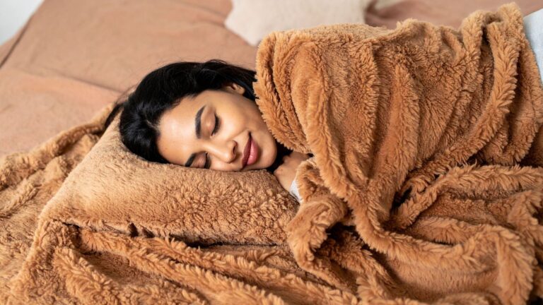 Femme allongĂ©e sous une couverture douce prĂšs dâune fenĂȘtre dâautomne, en quĂȘte de sommeil rĂ©parateur