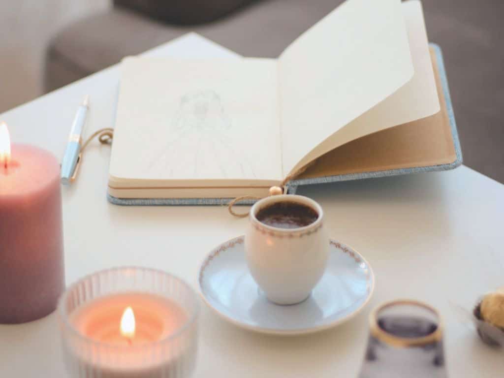 Carnet ouvert sur une table avec une tasse fumante et une bougie,  symbole de retour à l’essentiel et de clarté intérieure.